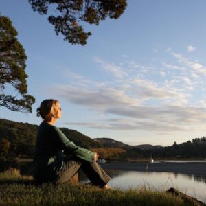 A woman sitting on the grass near a body of water.