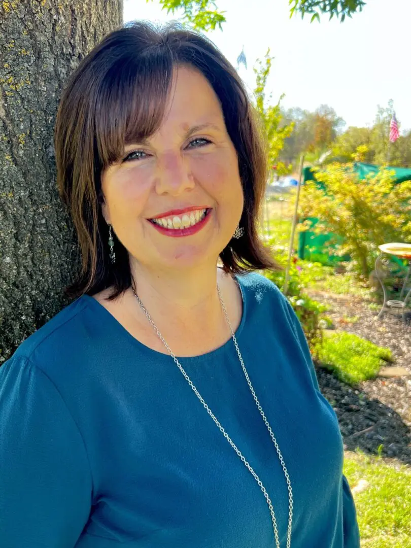 A woman standing in front of a tree smiling for the camera.