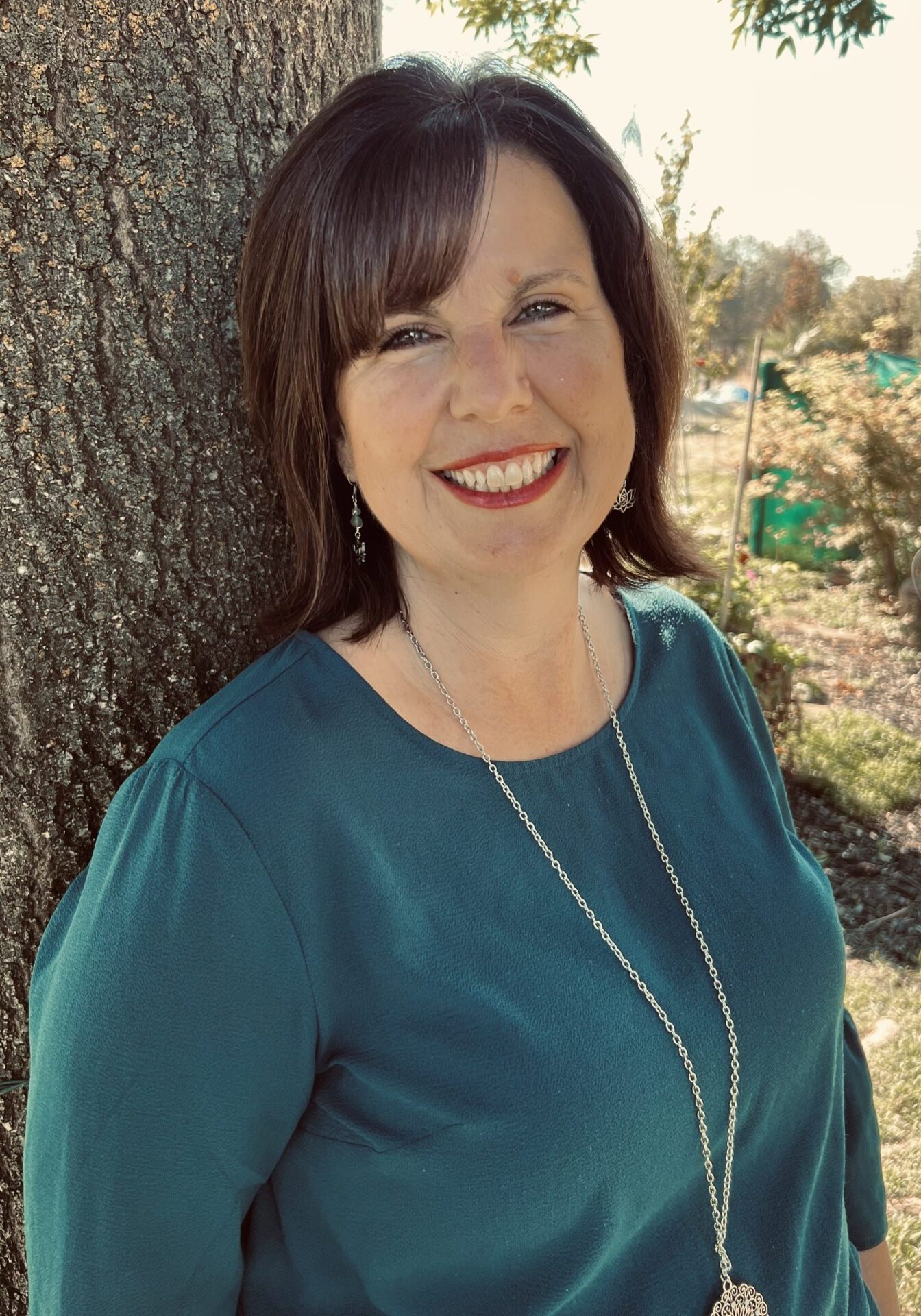 A woman standing in front of a tree smiling for the camera.